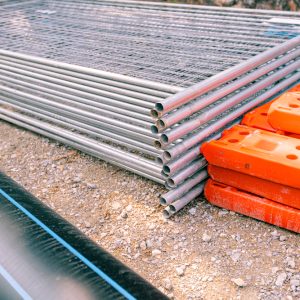 Pile, heap of galvanized parts for temporary metal fence panels are piled and hollow plastic fence foot on the street, ready for mounting around building site.